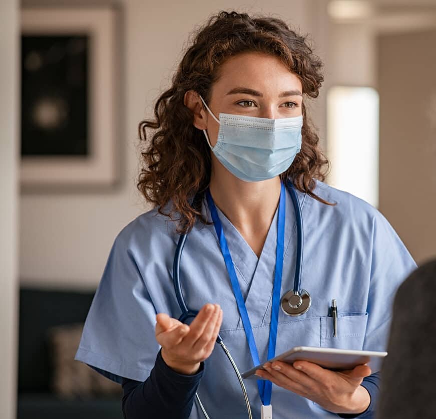 Female doctor holding digital tablet and wearing safety protective mask while talking to a woman about medical report