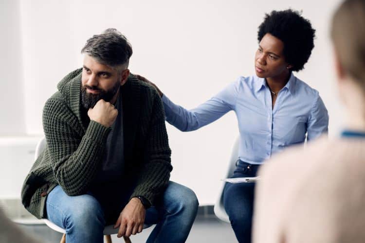 African American psychotherapist encouraging a man who is talking about his problems during group therapy. Focus is on man.