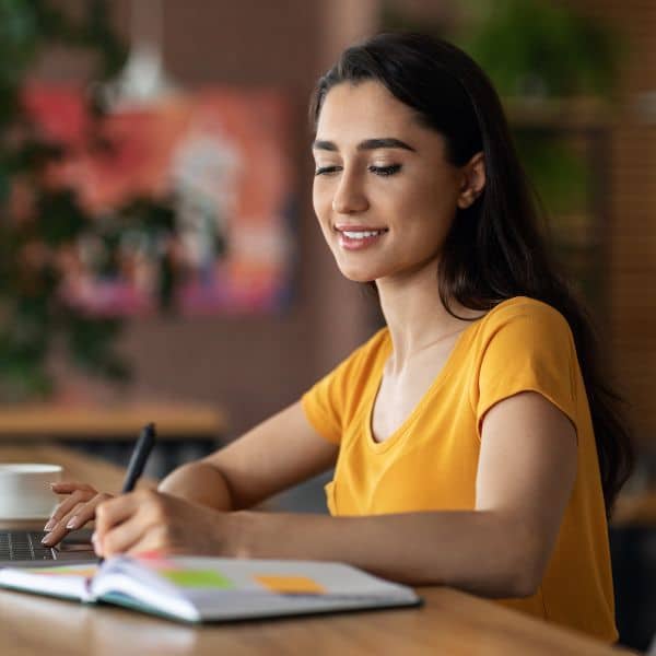 Young woman doing research online and taking notes in a notebook