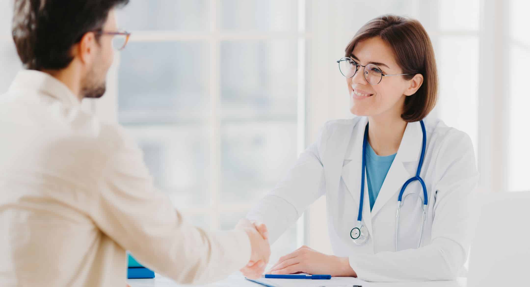 Friendly female doctor greets patient with handshake, pose in private clinic