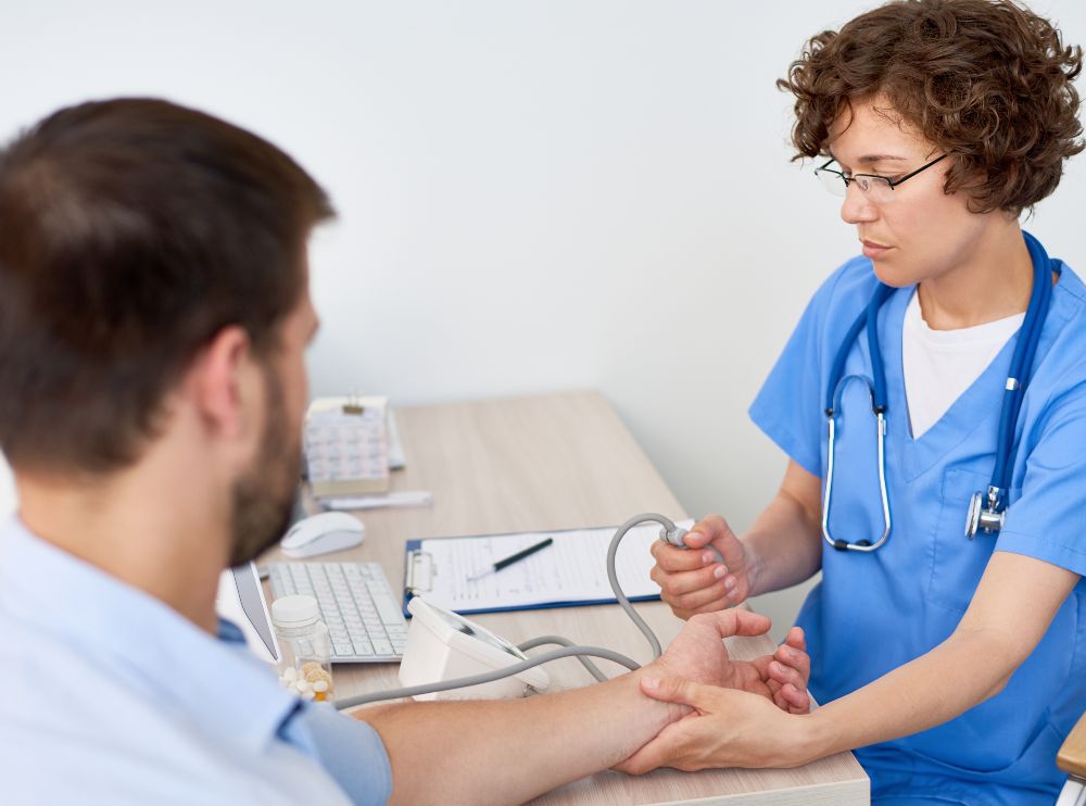 Portrait of young woman measuring patients blood pressure at desk in doctors office