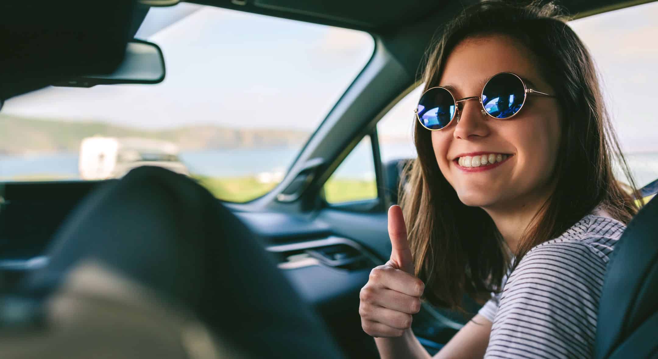 Young happy girl doing thumbs up in the car